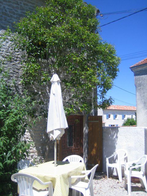 A garden table and chairs with white parasol outside a stone cottage