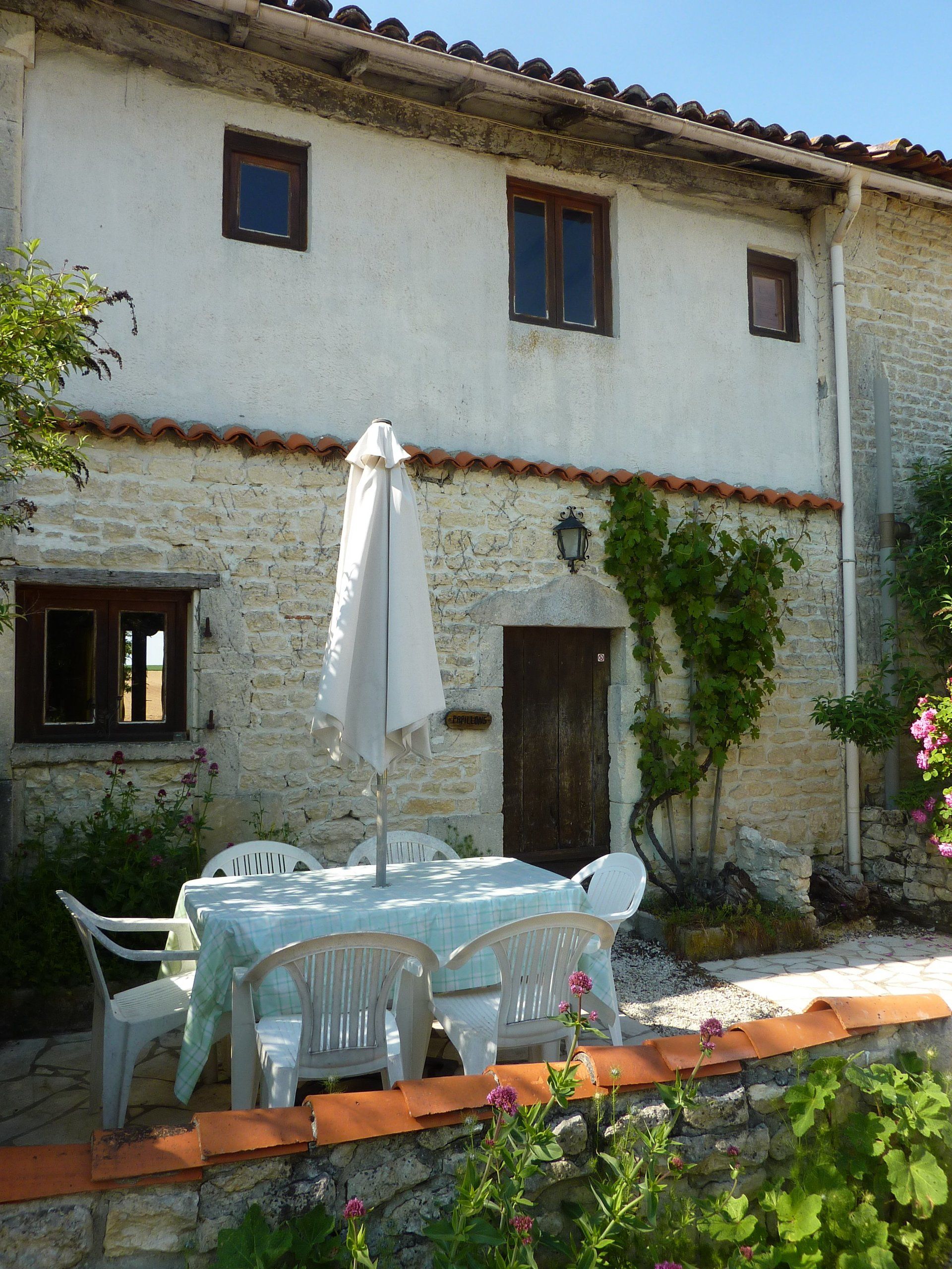 stone cottage with a plastic table and chairs outside and a white parasol