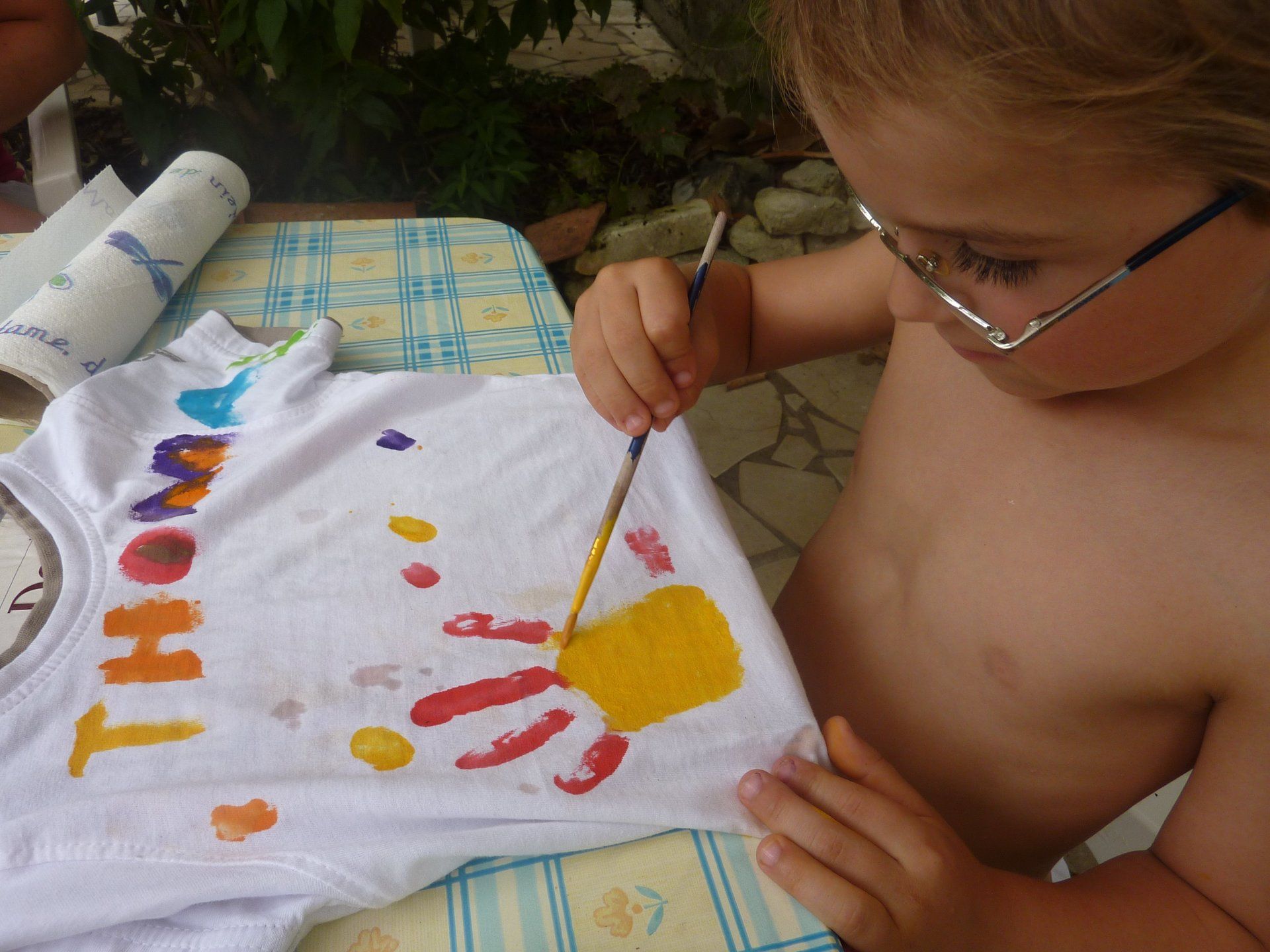 child painting a yellow hand with red fingers on a t-shirt
