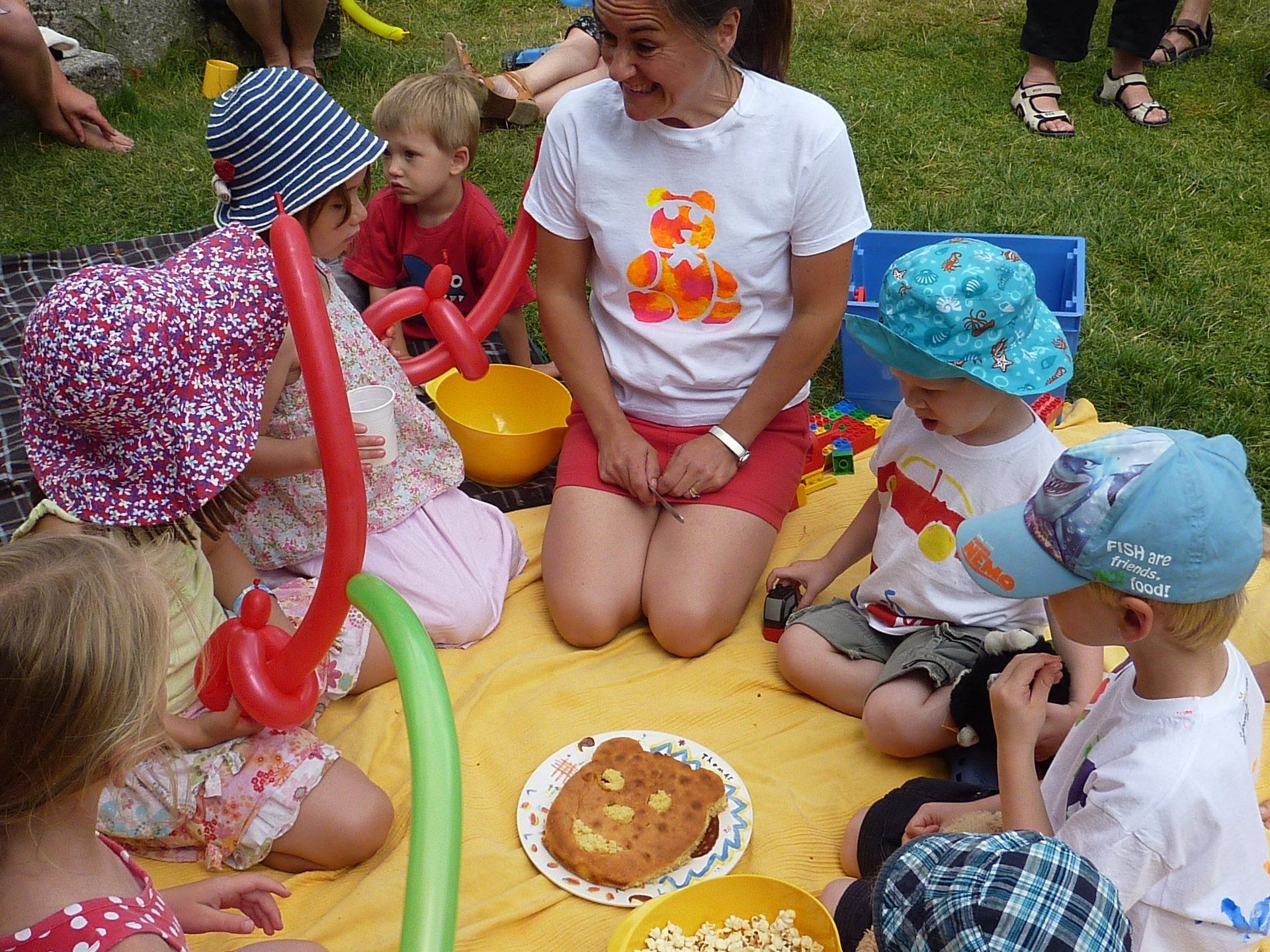 teddy bear picnic with children in a circle looking at a cake