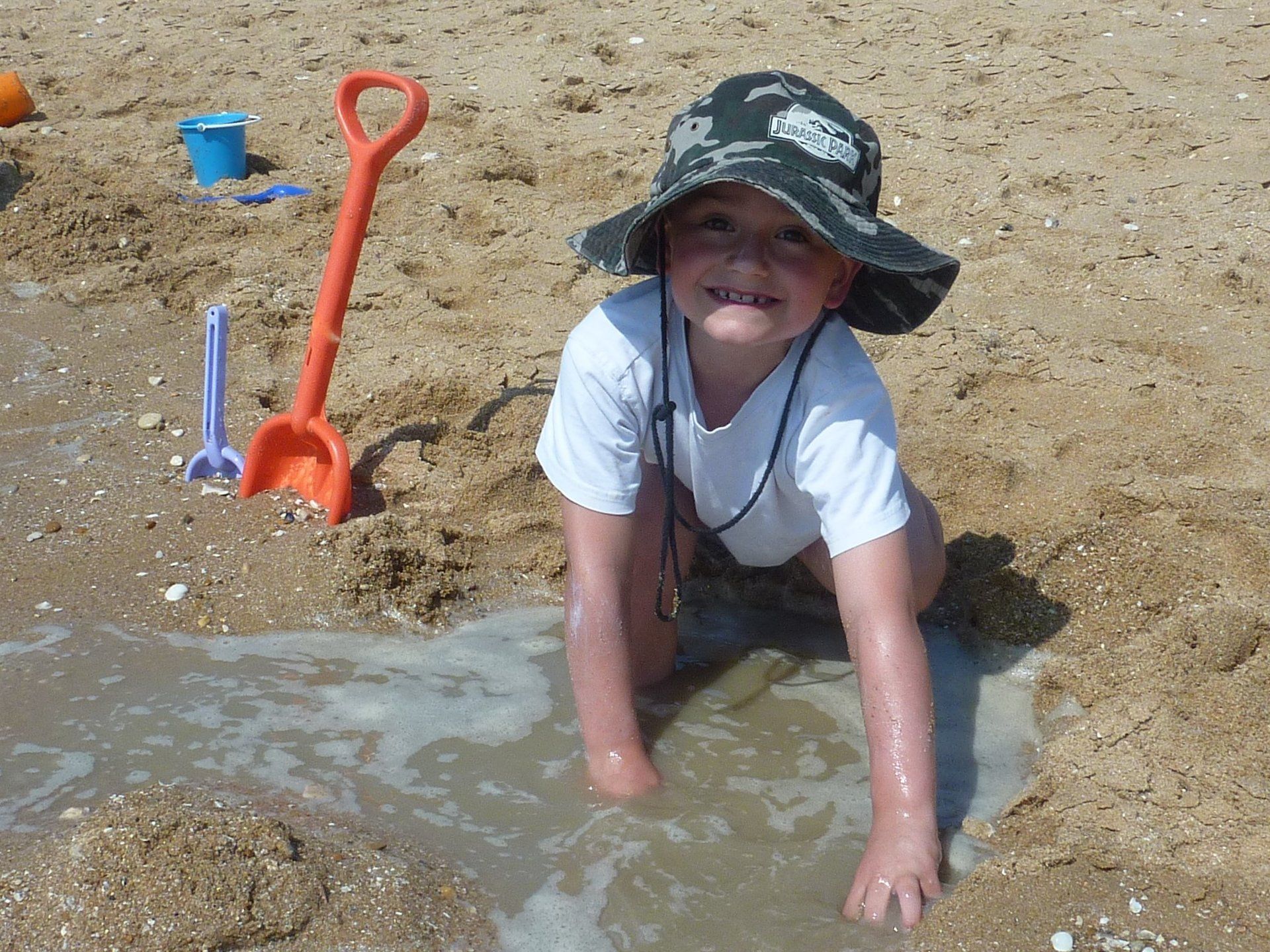 child playing in the sand digging a hole and seawater entering