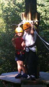 two boys with yellow helmets and safety harness at a rope park in the trees