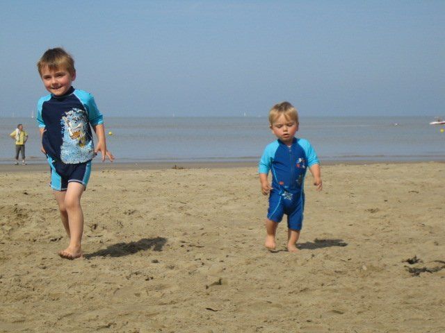 a young child and a toddler running on a sandy beach