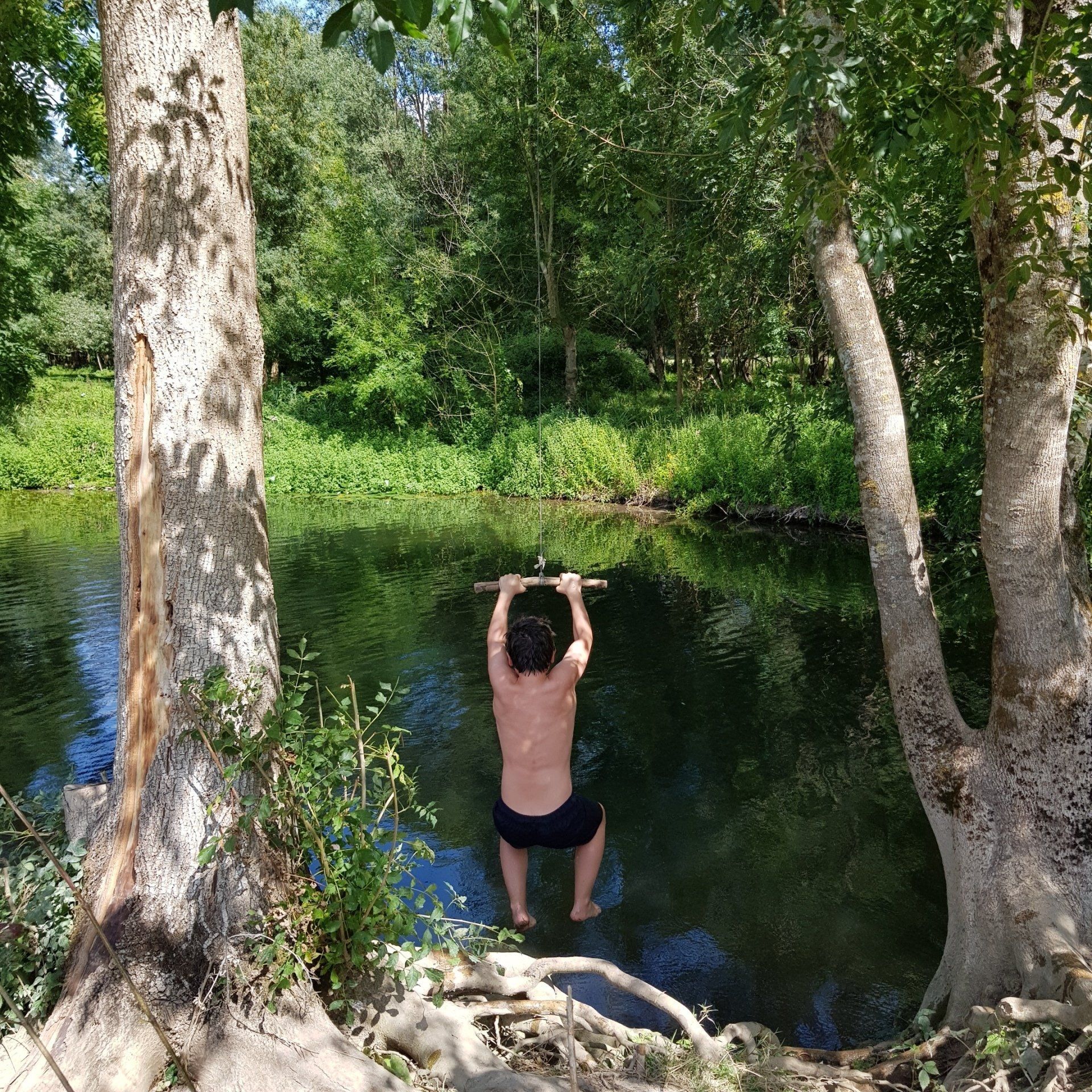 boy in swim shorts swinging into a river from a rope