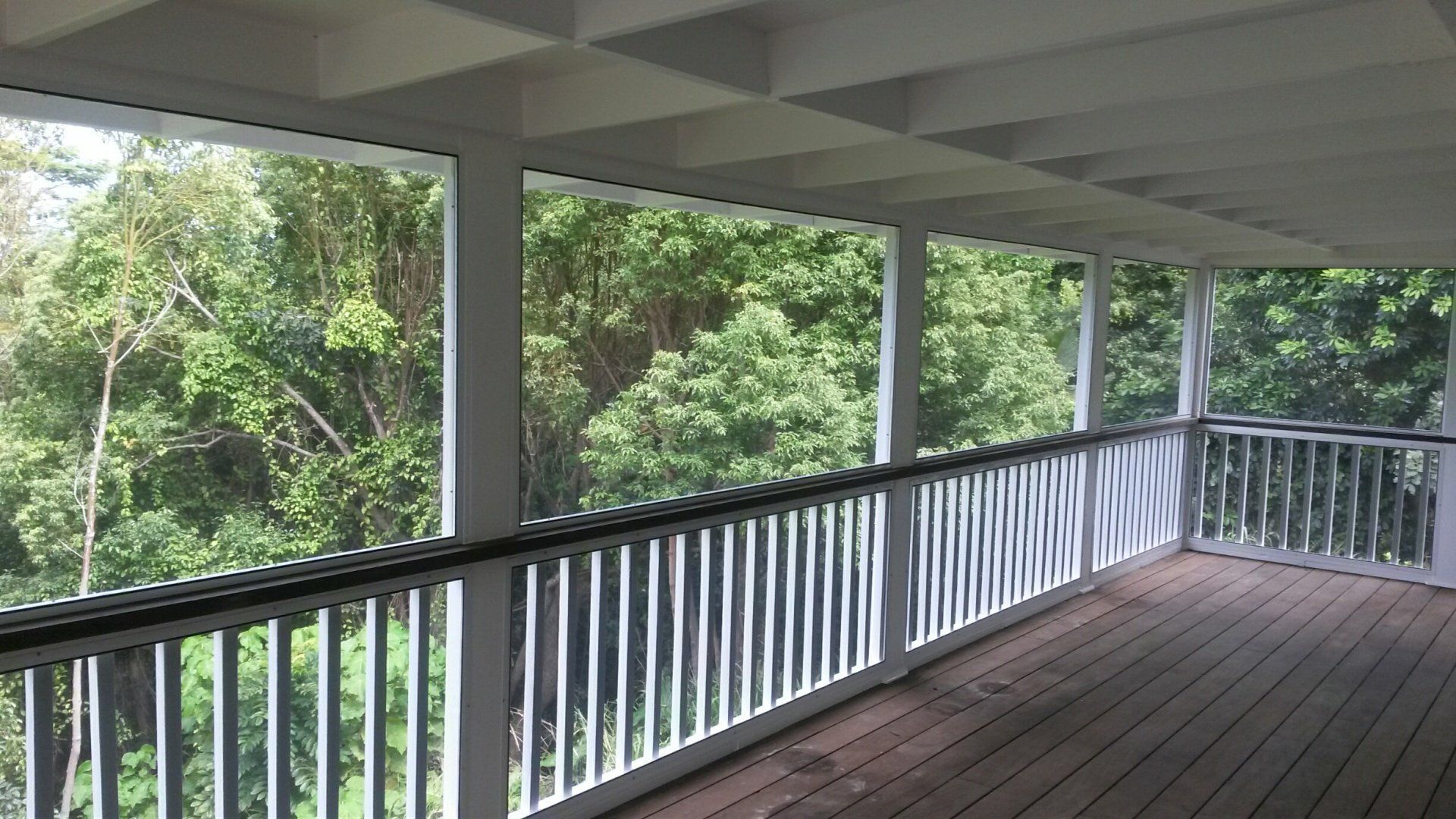 Covered porch with white railings, looking out at lush green trees.
