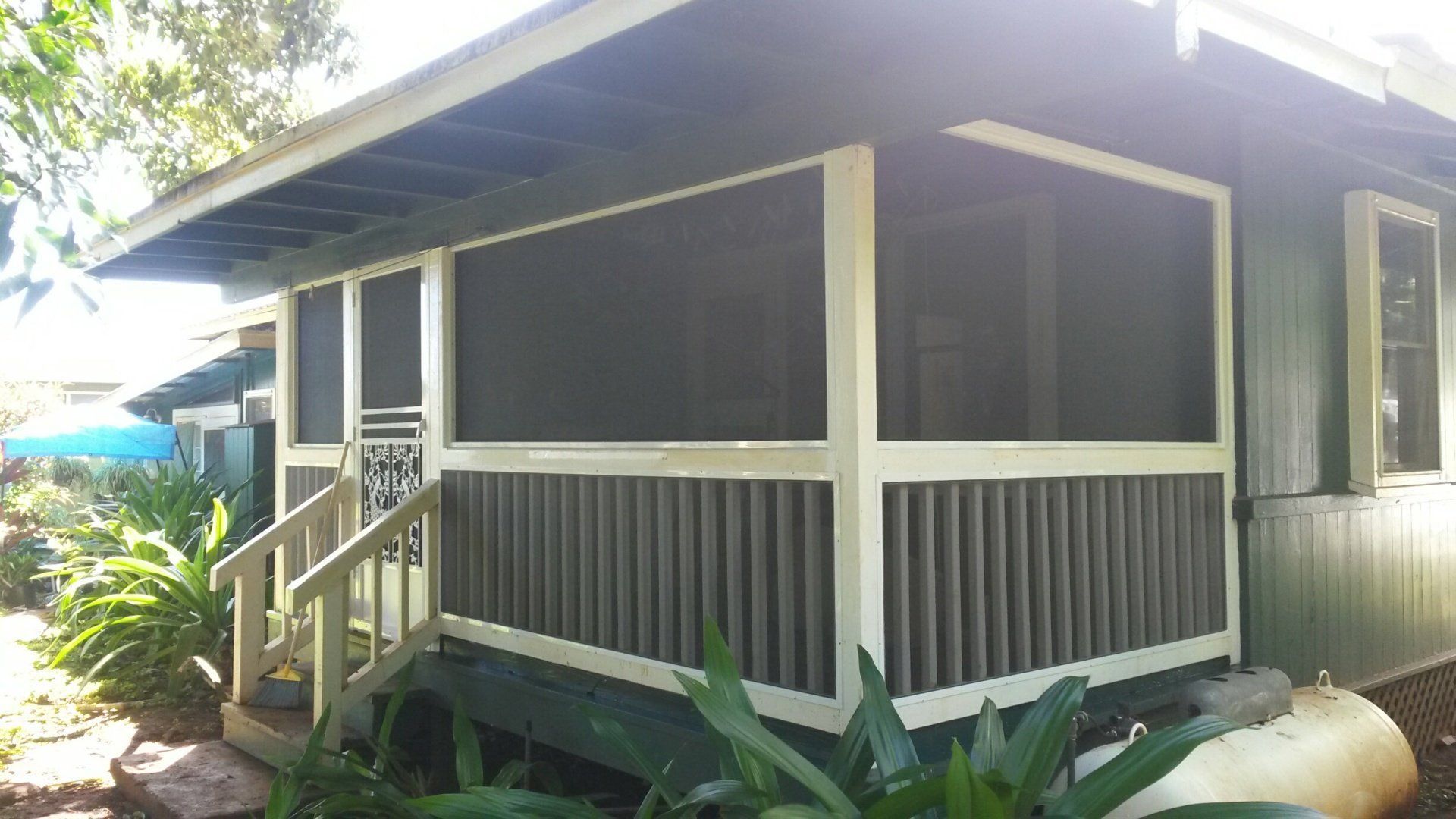Screened-in porch of a house, with vertical siding. Wooden railing, cream trim, and a small set of stairs.