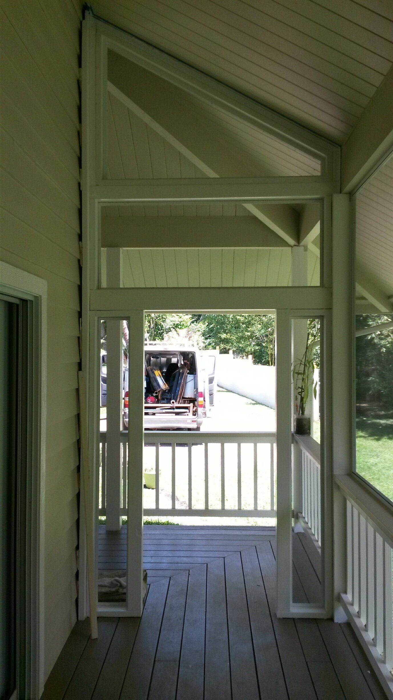 White-framed screen door on a wooden porch with a railing, leading to a yard with a parked truck.