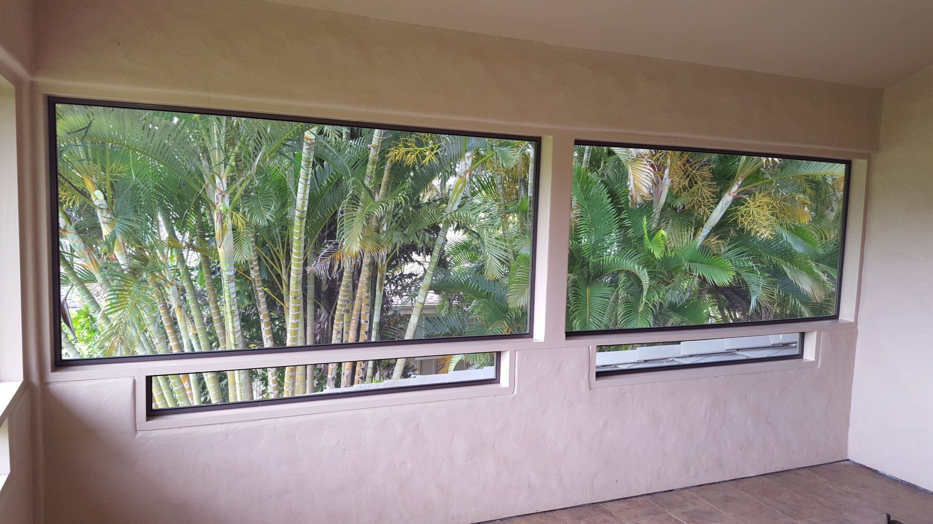 Two windows with black frames looking out at lush green trees. Beige walls.