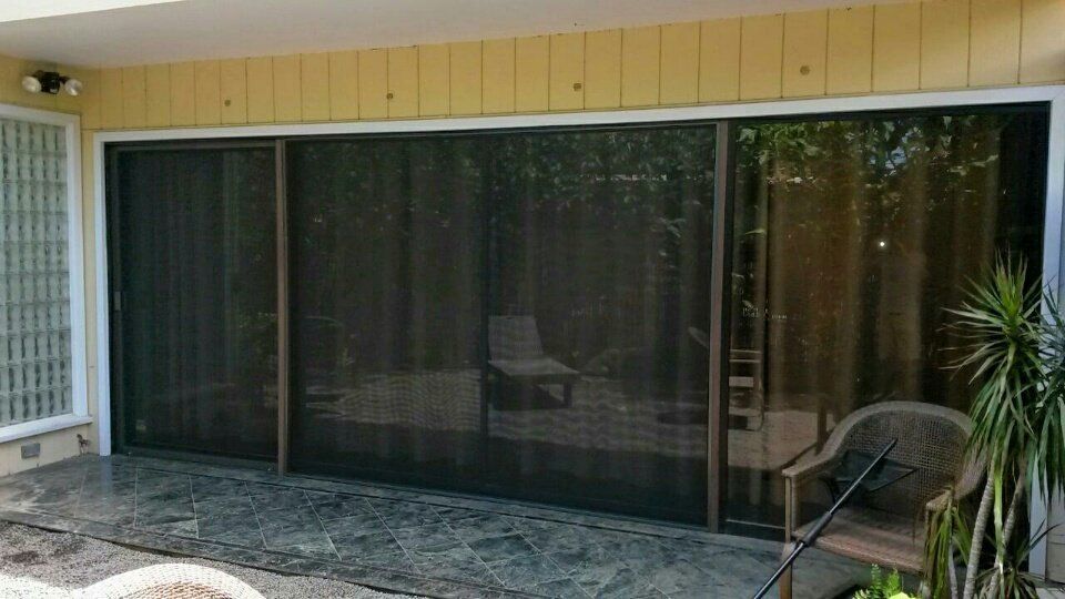 Sliding glass doors with a closed screen; brown frame and tan siding. Patio with wicker chair.