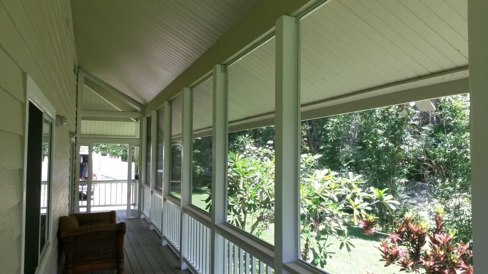 Covered porch with white pillars, railing, and retractable shades overlooking greenery.