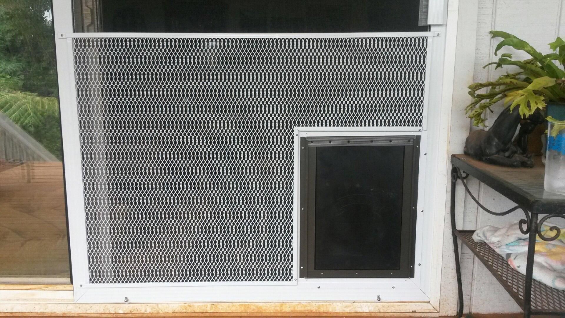 A screen door with a black and white geometric pattern and a pet door installed. A small table is to the right.