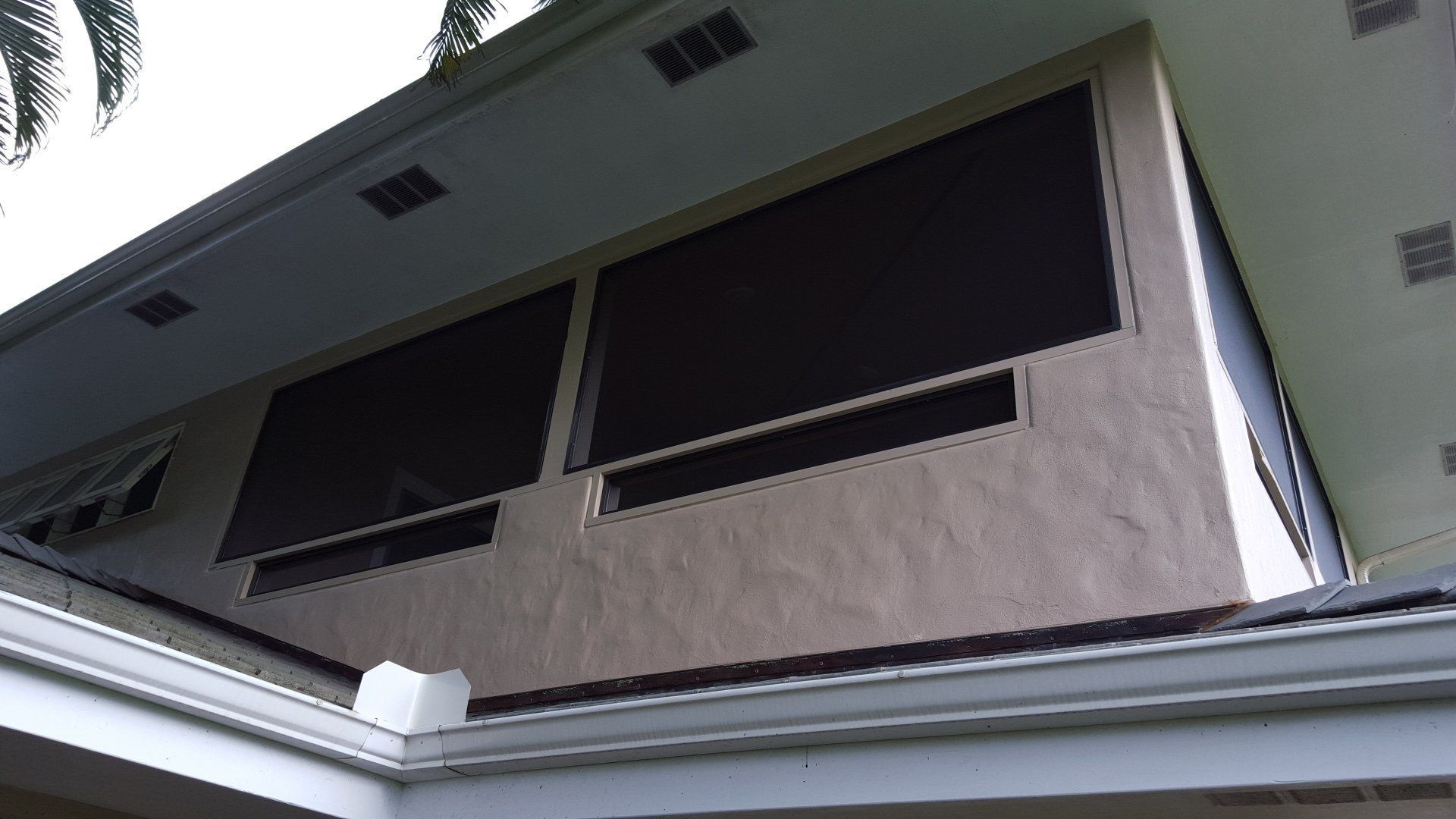 Exterior view of a building with dark-colored window screens. White roof and tan stucco walls.