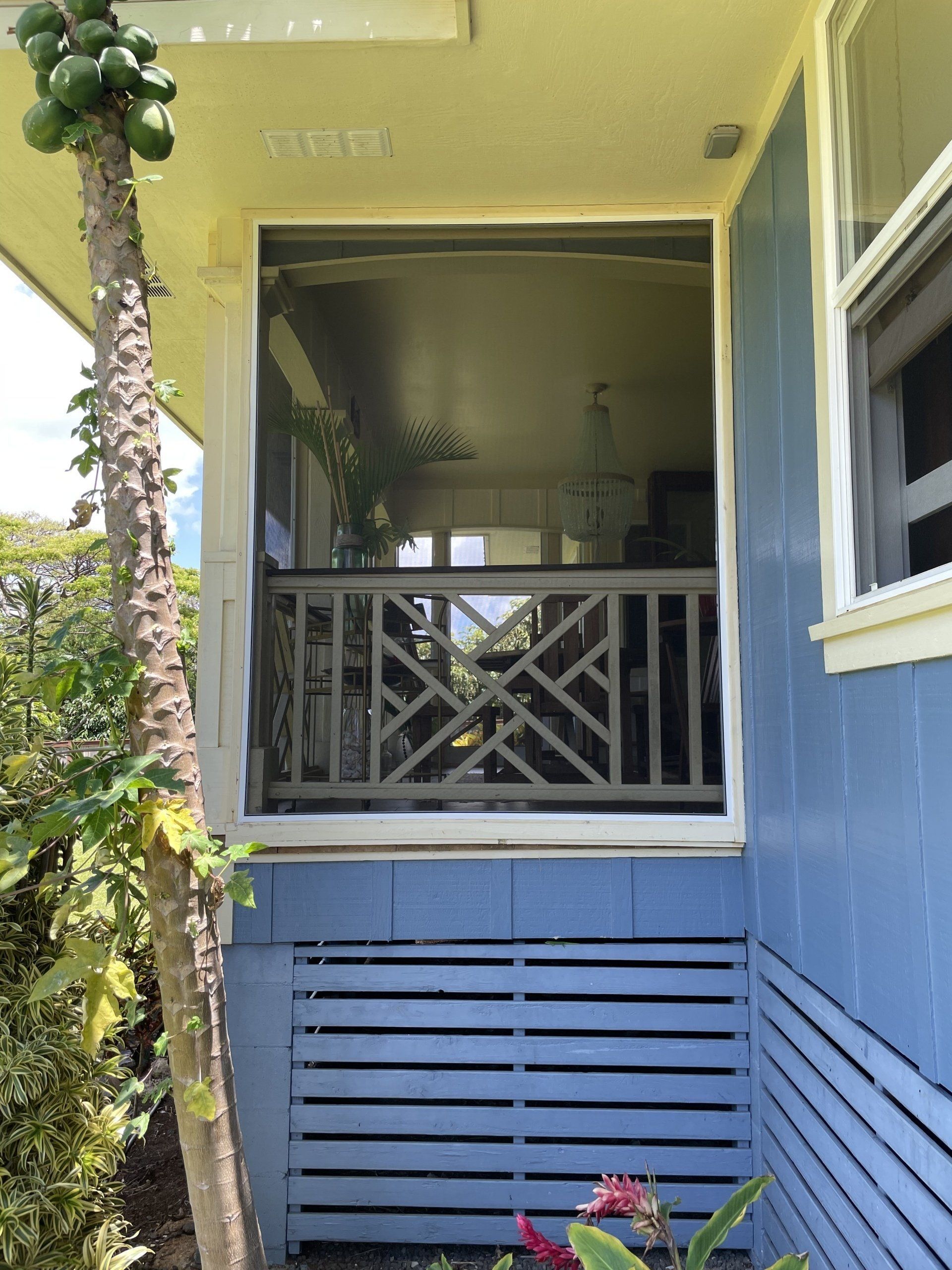 Blue porch with screen window, decorative railing, and papaya tree.