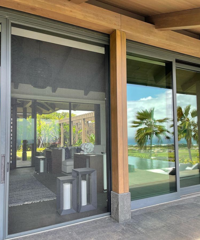 Sliding glass doors with a screen and view of an interior living area and tropical outdoor scenery.