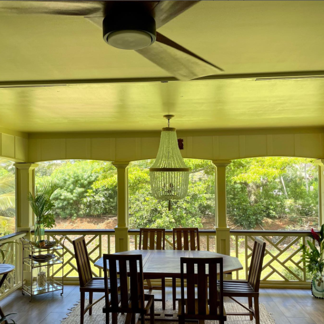 Covered outdoor dining area with a wooden table and chairs, chandelier, and a ceiling fan.