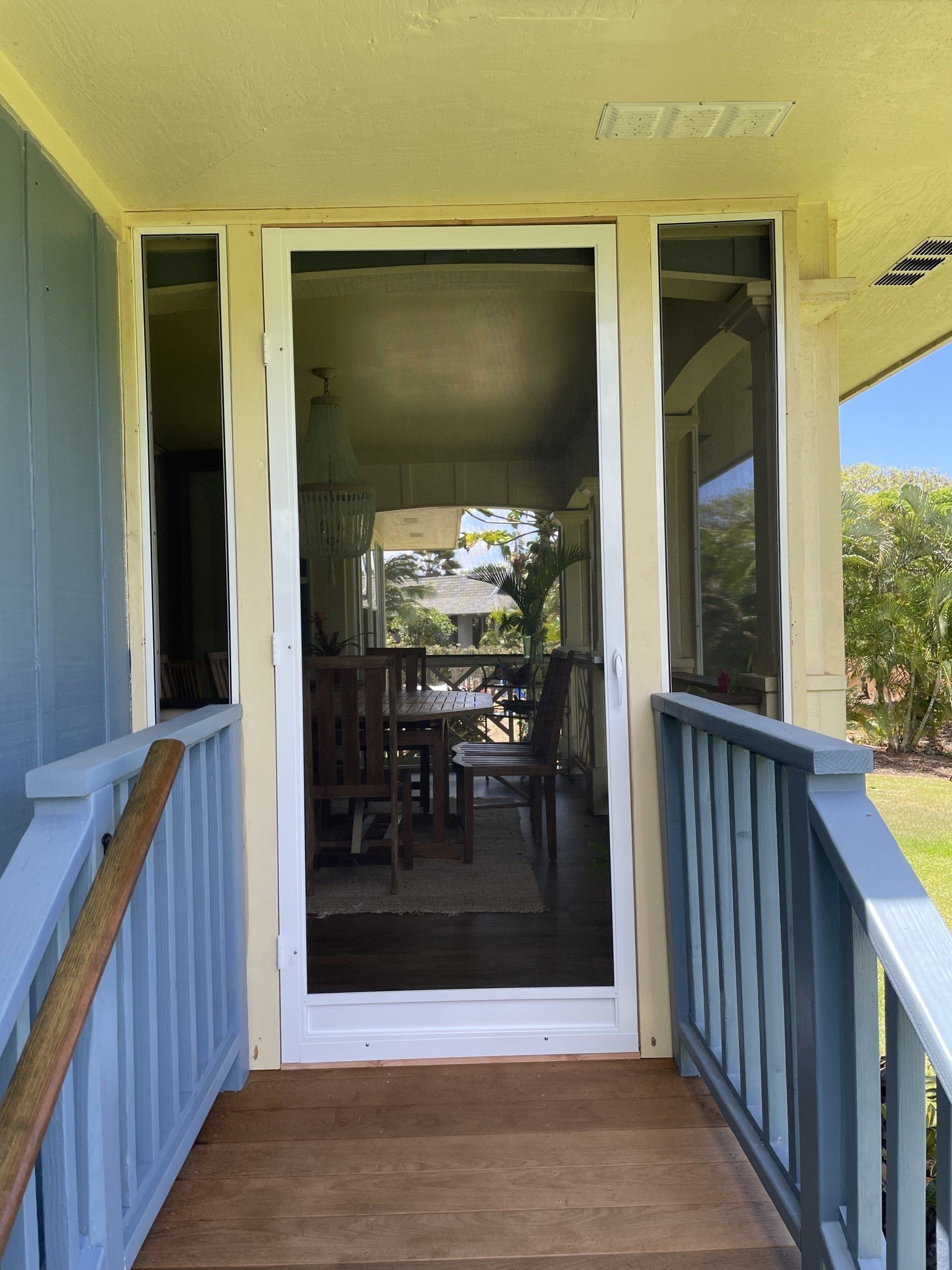 Screen door on porch, blue and white trim, leading to a room with a dining table.