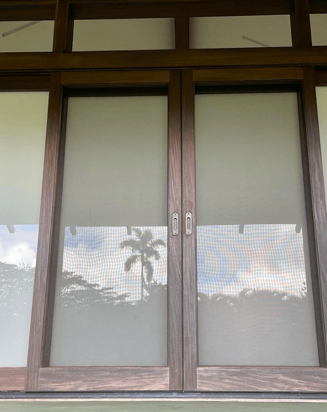 Wooden-framed glass doors with screens reflect a palm tree and sky.