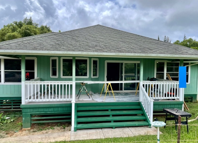 Green house with white railing, porch, and steps, cloudy sky.
