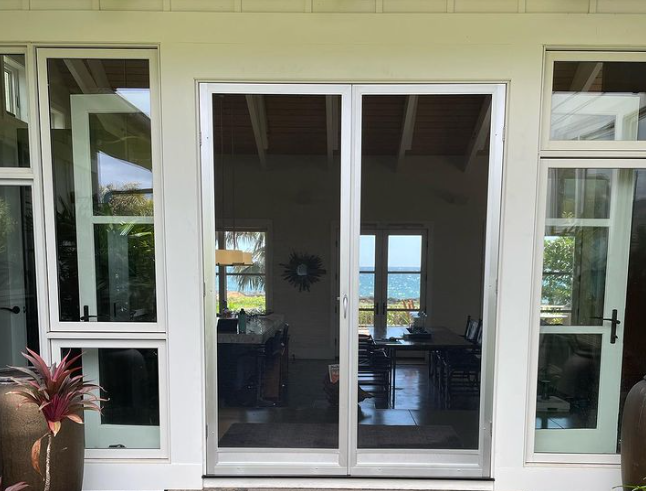 Exterior view: sliding glass door with screen, flanked by windows, set in white framing.