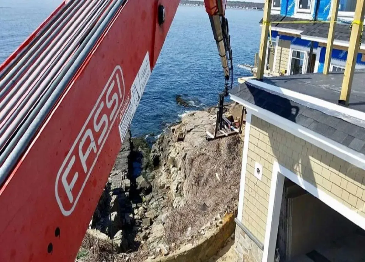 A red fassi crane is sitting on top of a building next to a body of water.