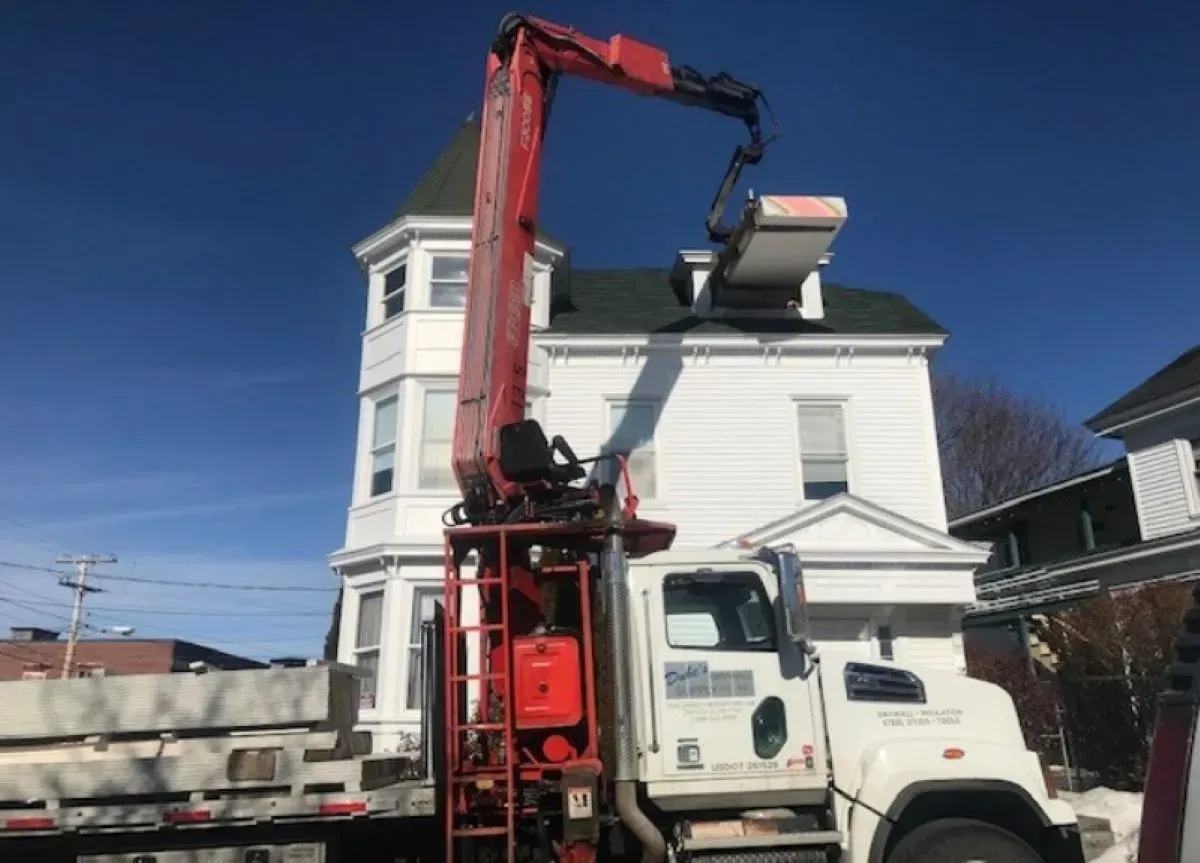 A truck with a crane attached to it is parked in front of a white house.