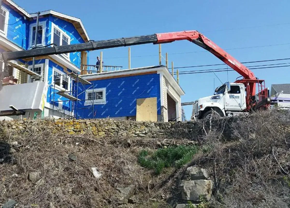 A truck with a crane attached to it is parked in front of a house under construction.