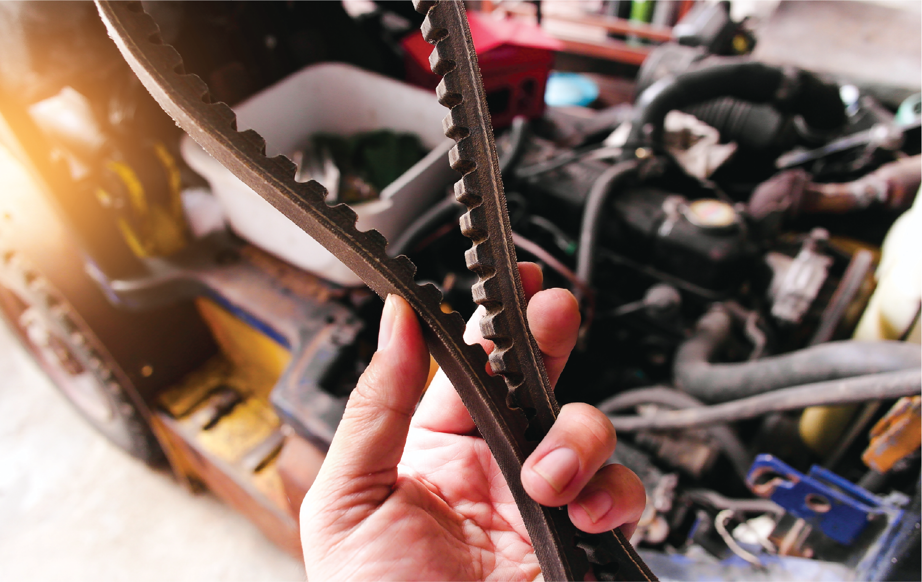 A person is holding a belt in front of a car engine.