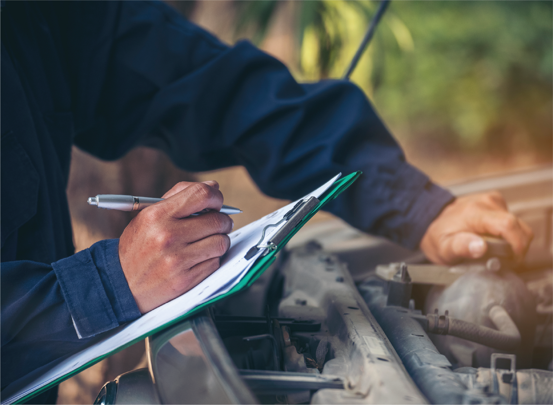 A man is writing on a clipboard while working on a car.