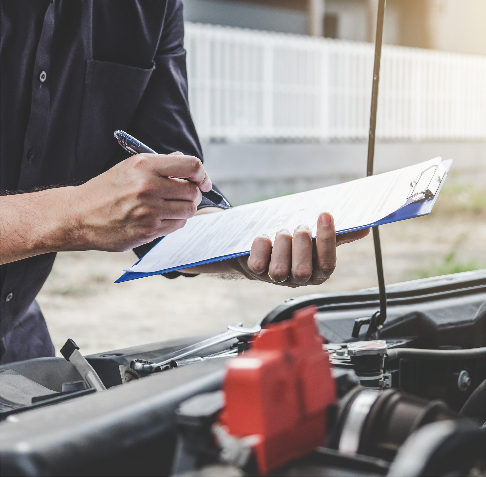 A man is writing on a clipboard while looking under the hood of a car.