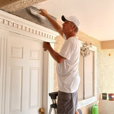 Person applying plaster to a wall with a trowel, wearing gloves, in a construction setting.