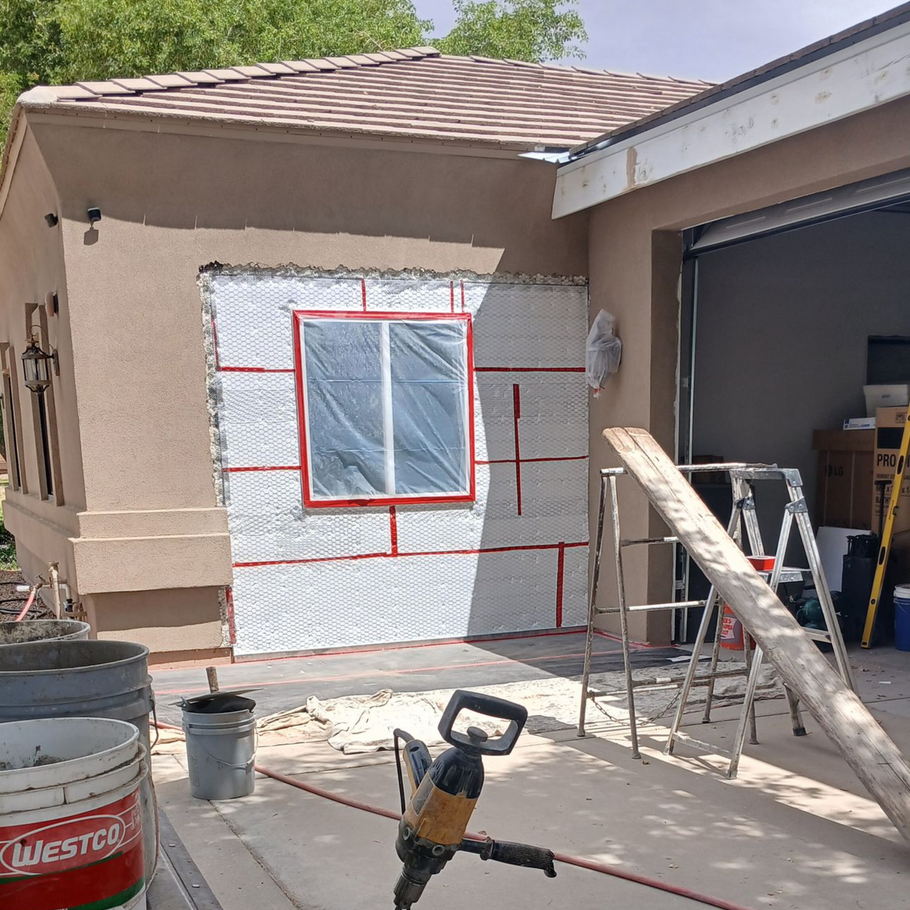 Person in work clothes applying stucco to a wall with a trowel.