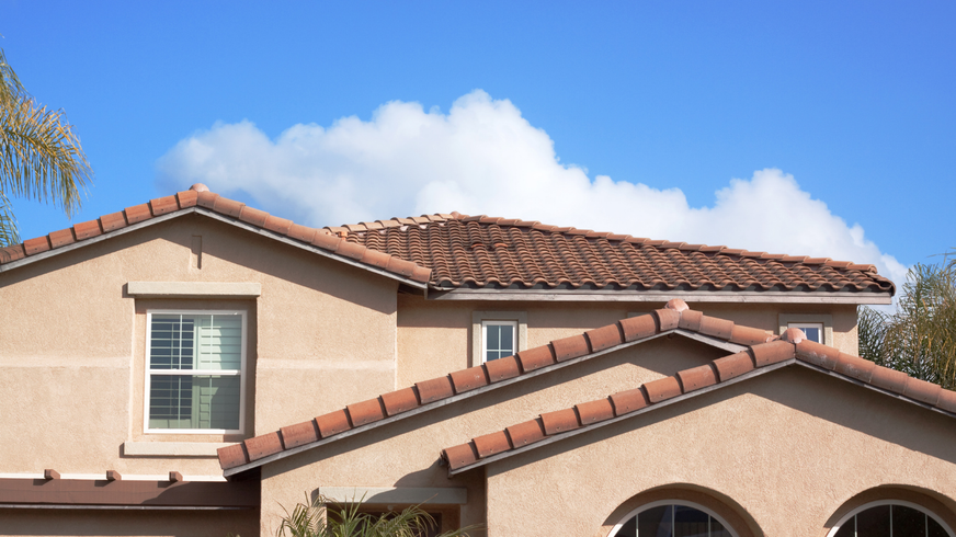 Tan stucco house with terracotta roof against a blue sky with white clouds.