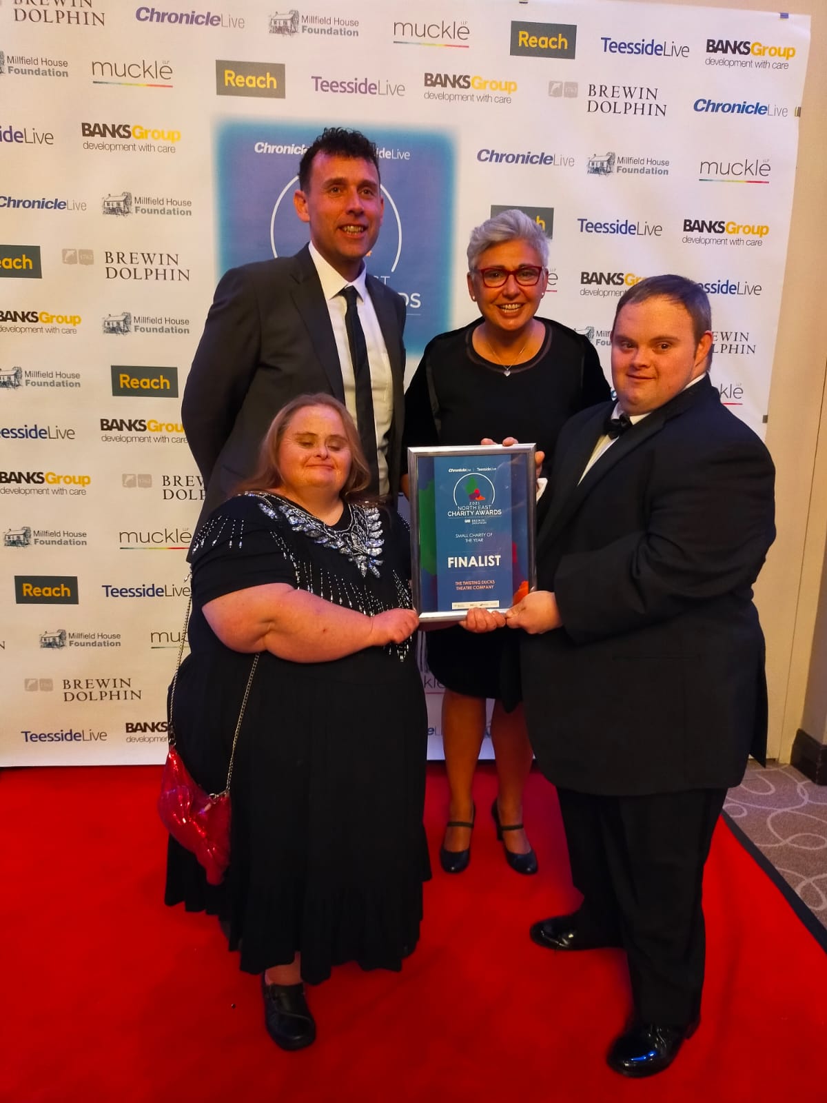 Jay and 3 other people from the twisting ducks, posing on a red carpet with their award in the 2021 North East Charity of the year award ceremony.