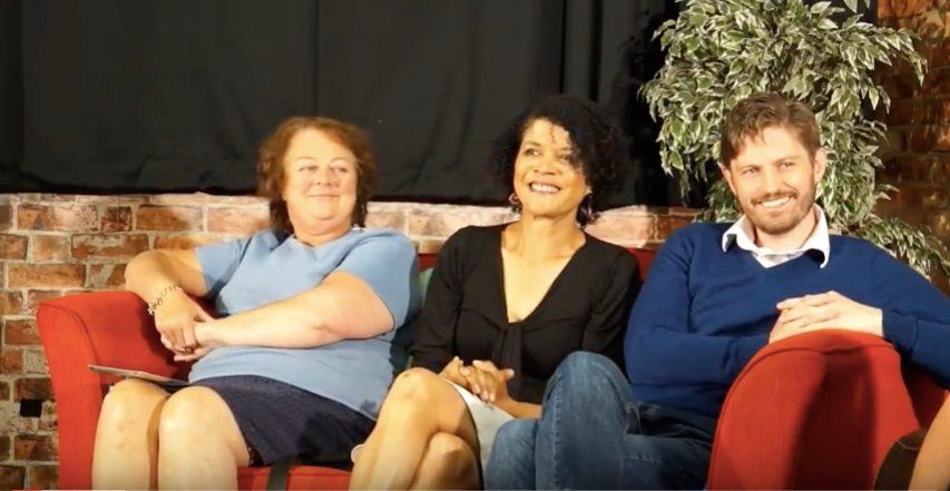 Two women and one man sitting, relaxed on a settee and smiling.