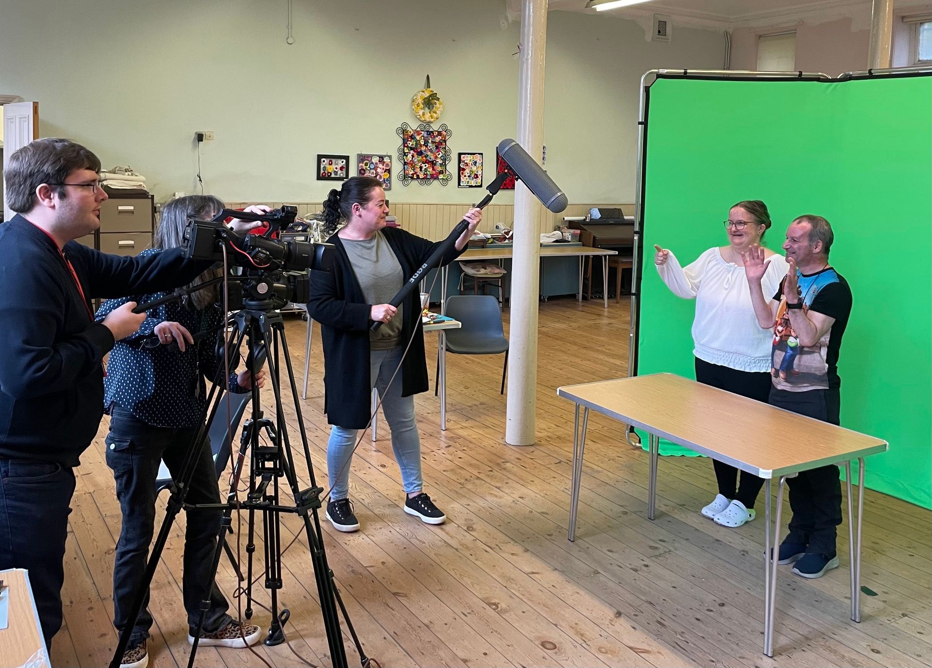 Photograph of a man and woman stood in front of a green screen being filmed on camera