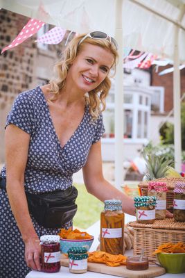Woman smiling at a market stall with jars of food and decorative bunting.