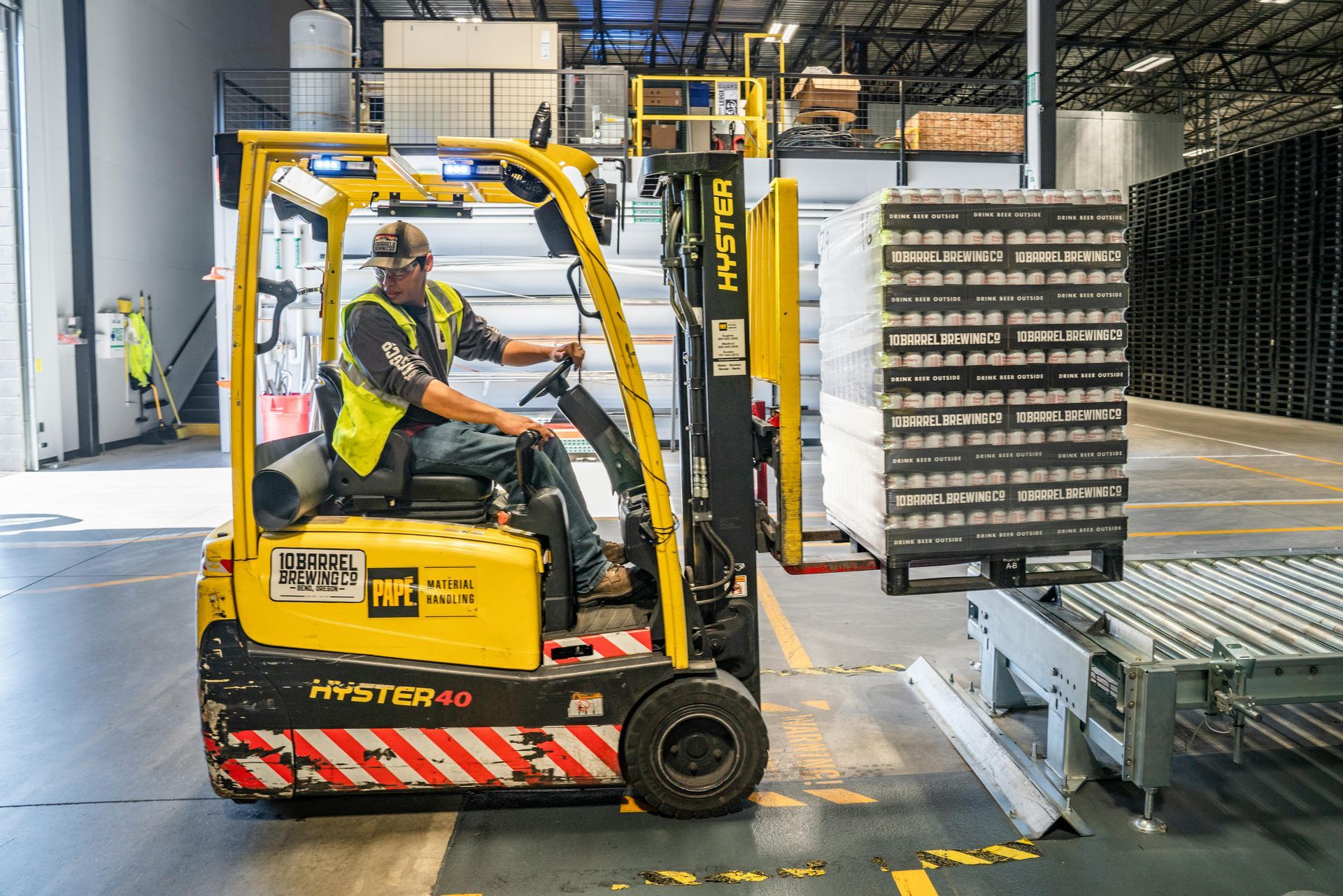 Forklift operator in a warehouse, moving stacked pallets.