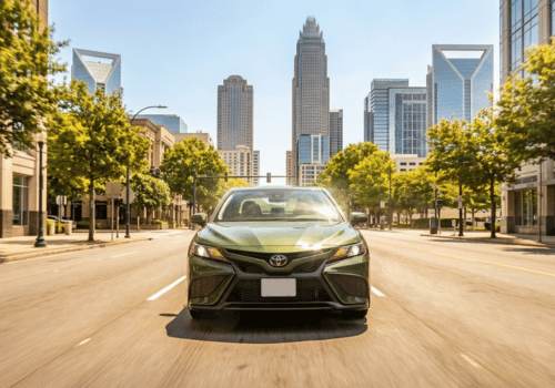 Front-facing view of a Toyota sedan driving through a modern downtown city with a skyline of high-rise buildings in the background.