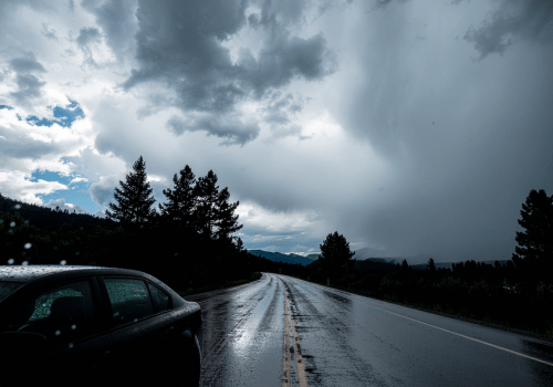 Wet highway under dark storm clouds with a car on the roadside, highlighting rainy driving conditions and reduced visibility.