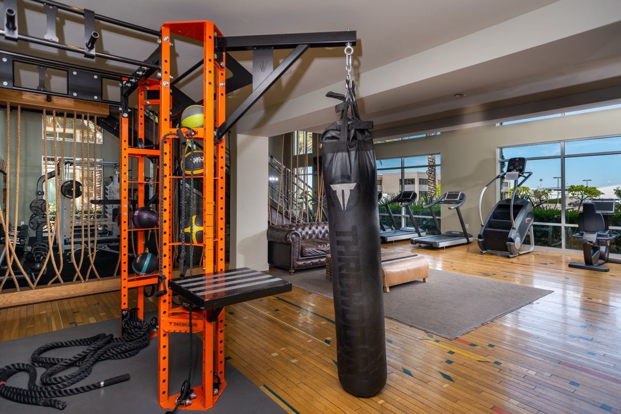 Modern gym with orange power rack, punching bag, ropes, and cardio machines.