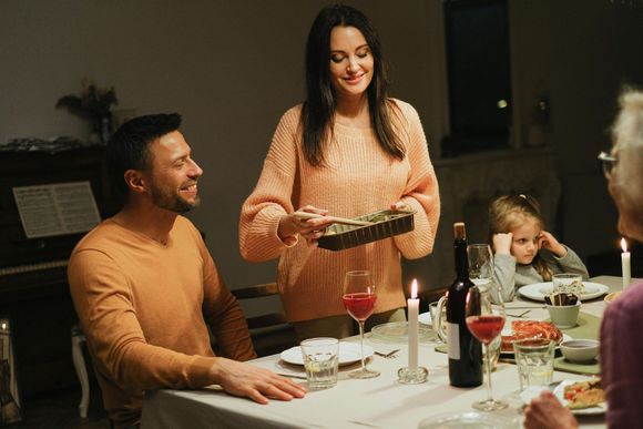 Woman serving food at a candlelit dinner. Man smiles, child looks bored. Setting is a dining room.