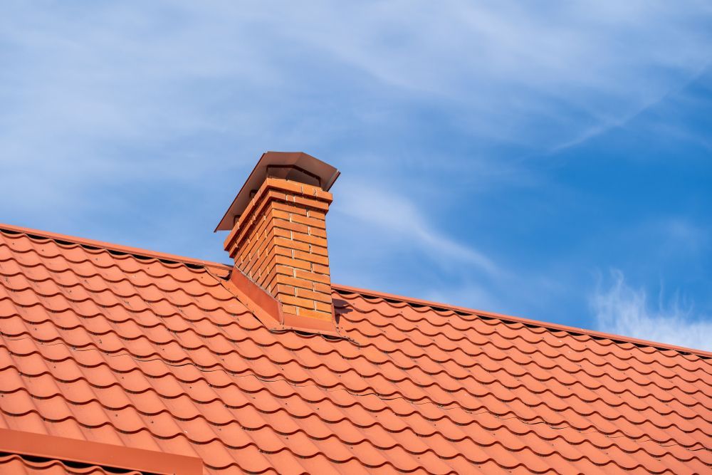 Red Tiled Roof With Brick Chimney Against a Blue Sky — CP Roofing in Old Bar, NSW