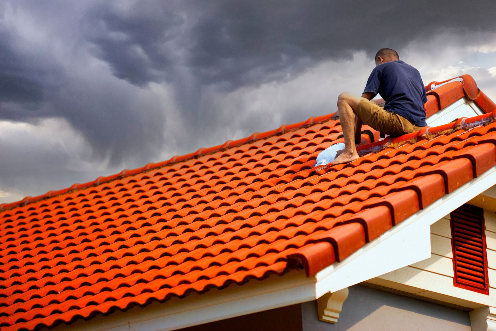 Man on Orange Tiled Roof, Dark Storm Clouds Looming — CP Roofing in Old Bar, NSW