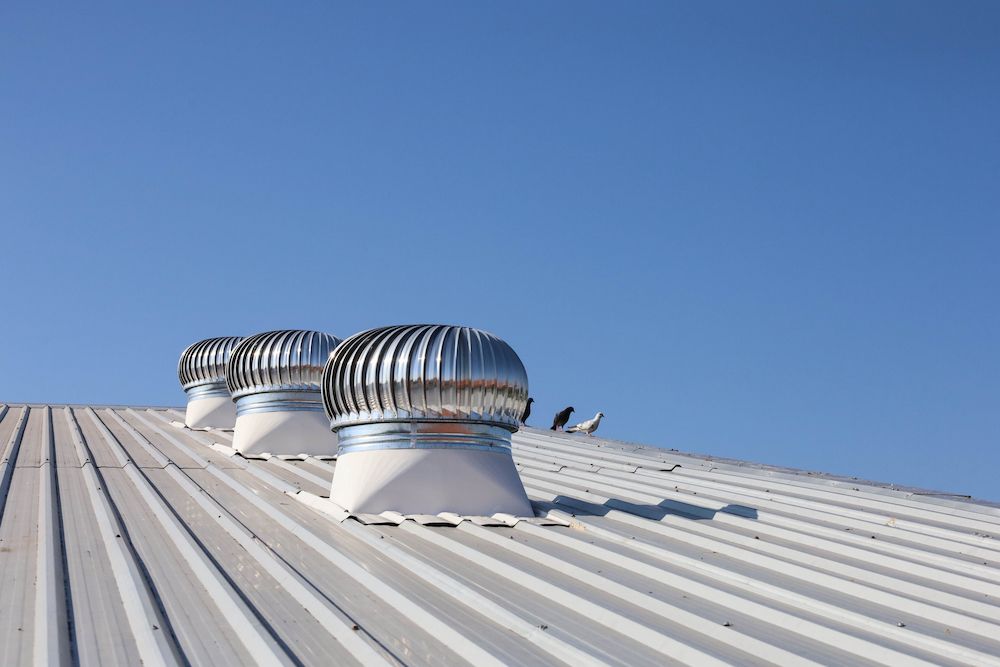 Three Silver Roof Vents on a Corrugated Metal Roof Under a Clear Blue Sky — CP Roofing in Old Bar, NSW