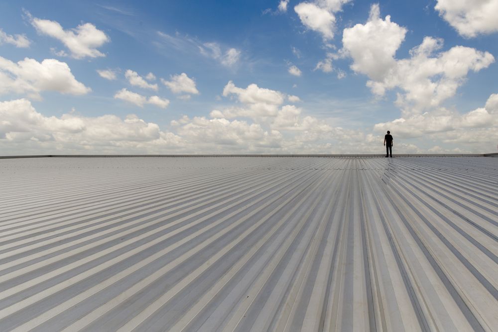 Person Standing on a Large, Reflective Metal Surface Under a Cloudy Blue Sky — CP Roofing in Old Bar, NSW