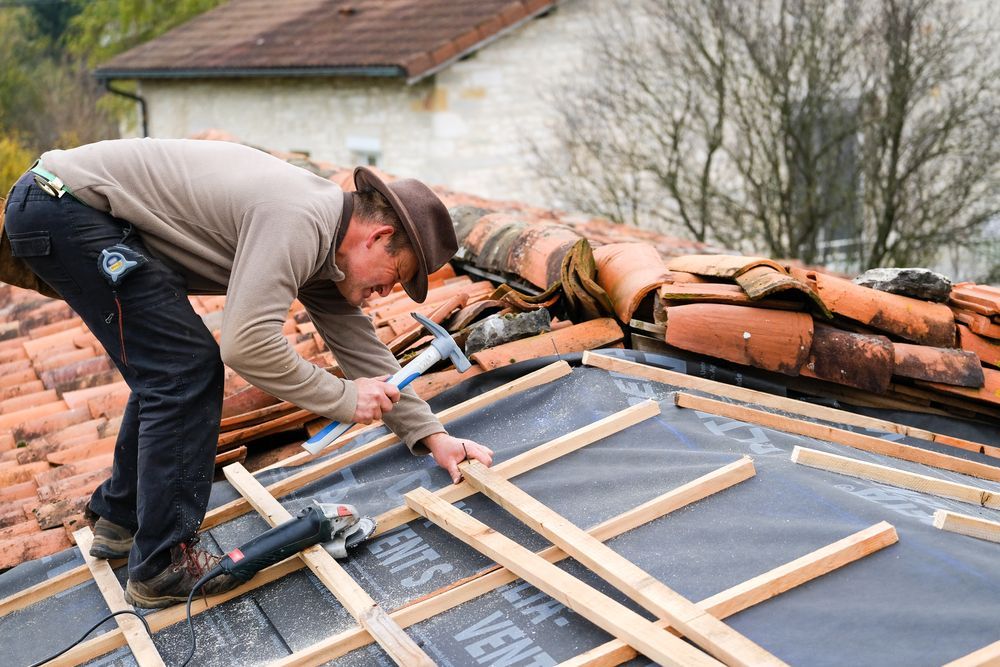 Man in Hat Hammers on Rooftop, Laying Wooden Framework Over Dark Underlayment — CP Roofing in Old Bar, NSW