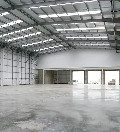 An Empty Warehouse With A Concrete Floor And A Metal Roof — CP Roofing in Old Bar, NSW