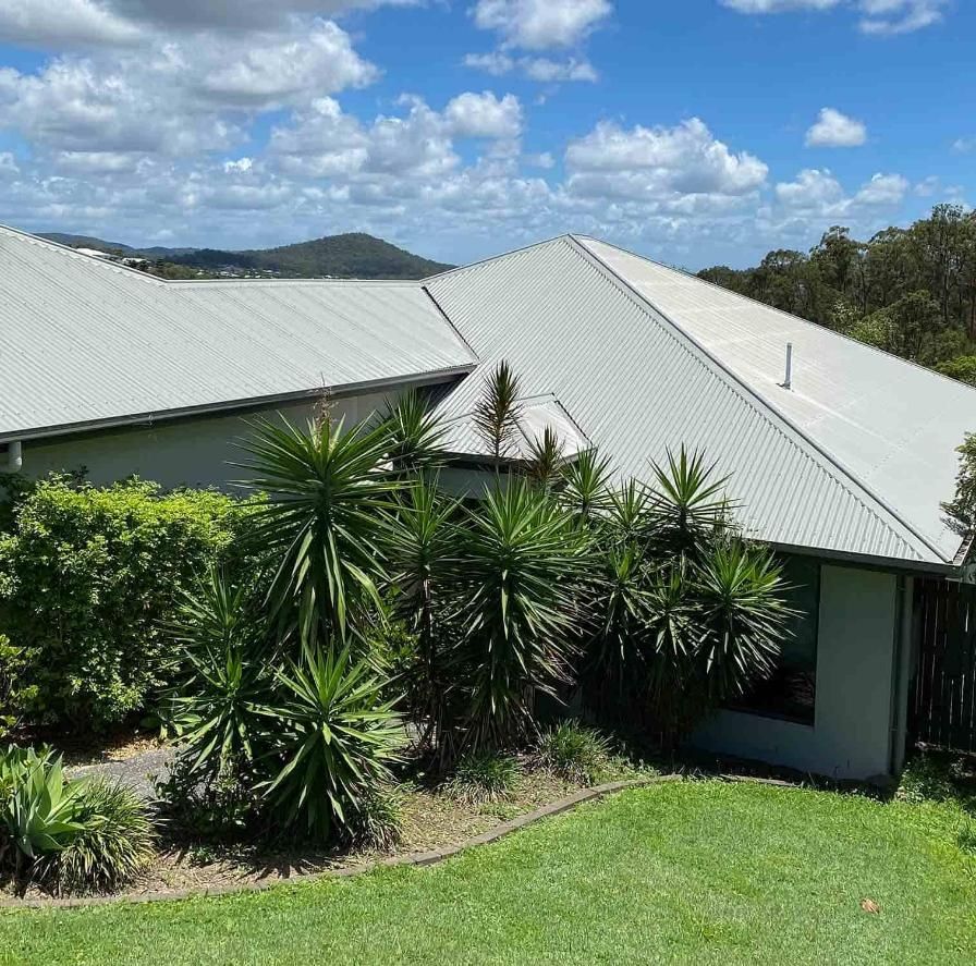 A House With A White Roof Is Surrounded By Trees And Bushes — CP Roofing in Old Bar, NSW