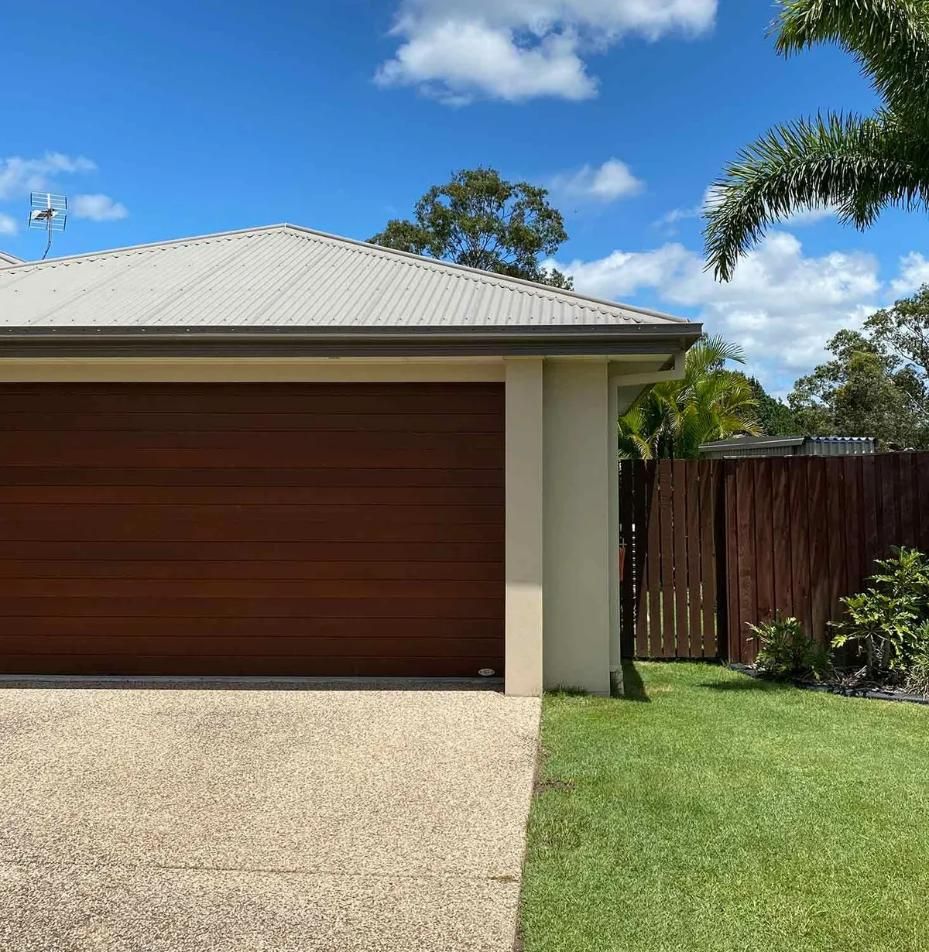 A House With A Wooden Garage Door And A Gravel Driveway — CP Roofing in Wingham, NSW