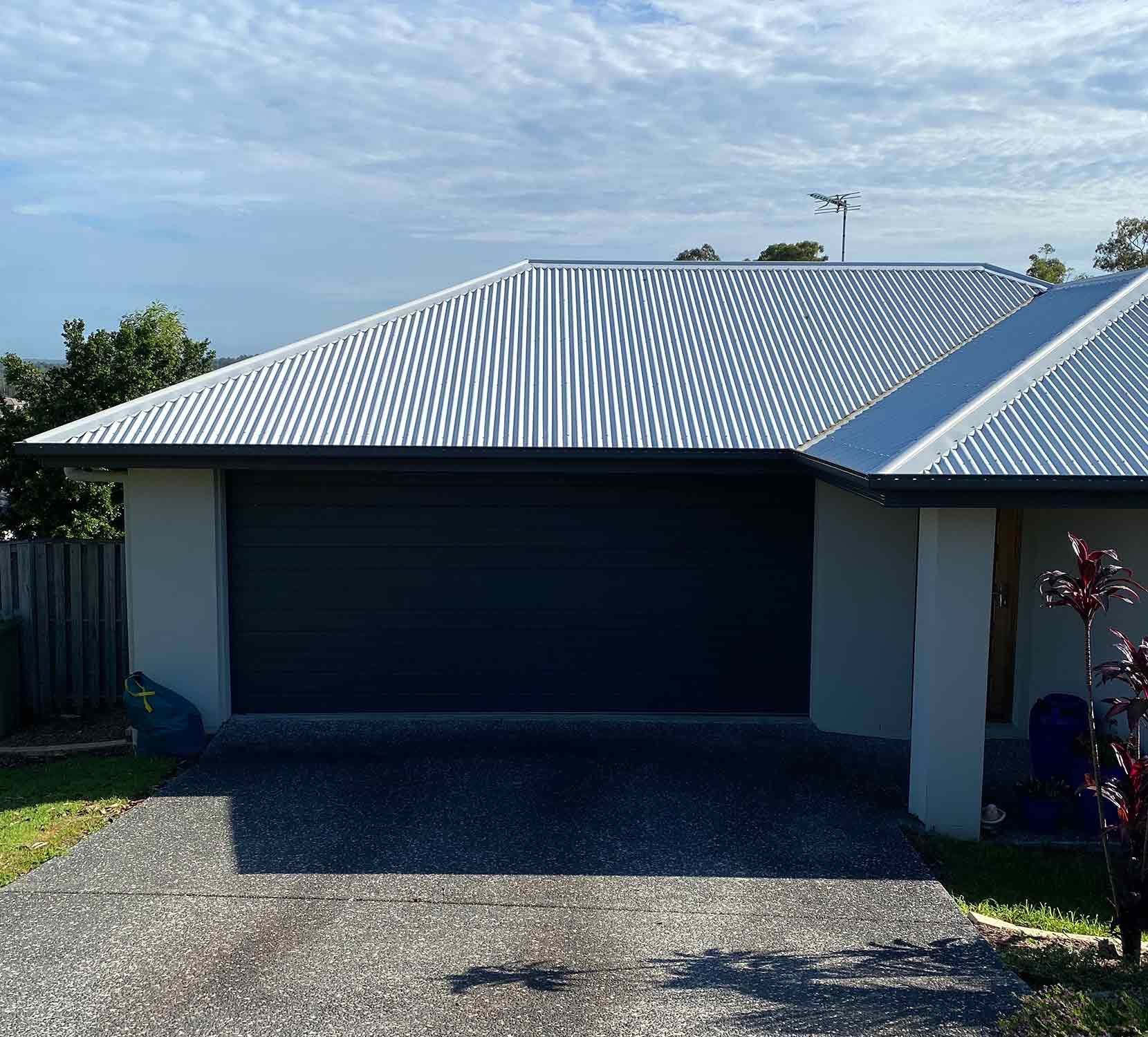 A White House With A Black Garage Door And A White Roof — CP Roofing in Taree, NSW